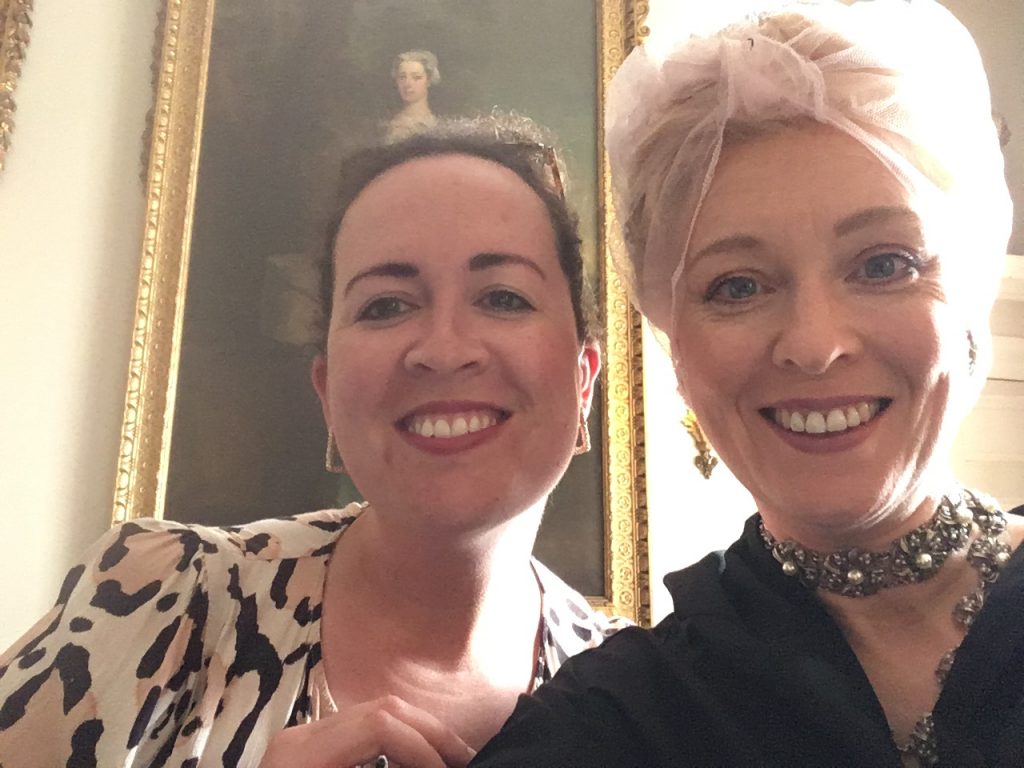 Camilla and Sophie selfie. Camilla is in modern clothes, Sophie in costume as Lady Stowell in a behind the scenes Bridgerton photo, wearing a protective hair net and black privacy cloak. 